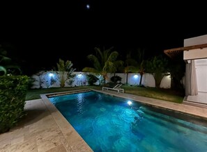 A nighttime swimming pool with clear water, surrounded by a well-lit garden and a white building. - Villa La Paisible de Palm Grove 2 (Grand Baie)