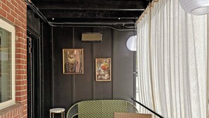 Un pequeño espacio al aire libre con una silla de mimbre, una mesa, una planta en maceta y un cuadro en la pared.
