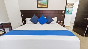 Un letto grande con una coperta bianca e azzurra, una testiera scura e tre cuscini blu.