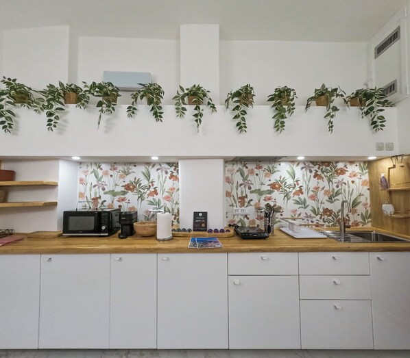 Une cuisine moderne avec des meubles blancs, un plan de travail en bois, un four à micro-ondes, une machine à café et un évier.