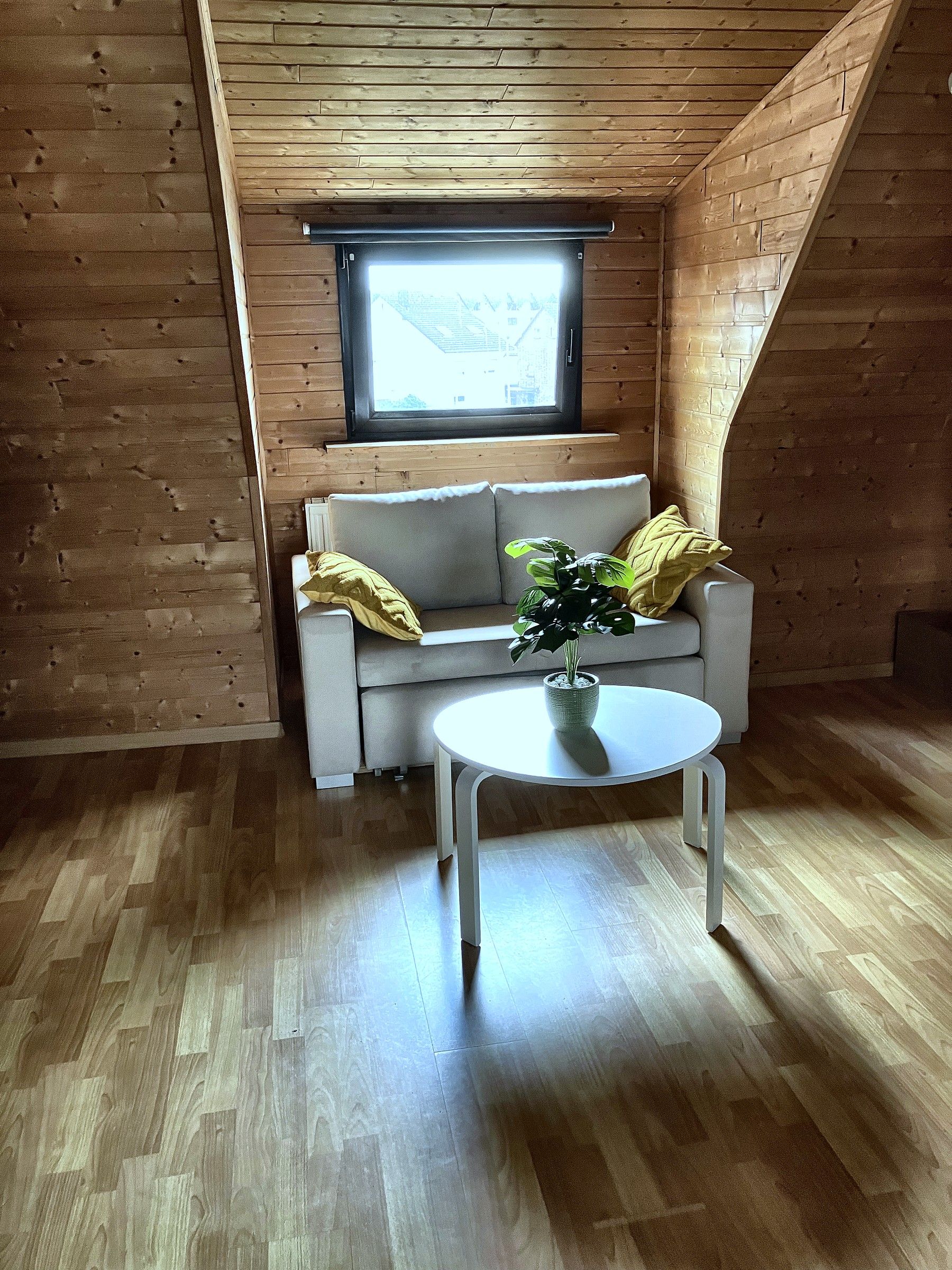 Ein Zimmer mit Holzbalkendecke, einer Couch, einem kleinen runden Tisch und einem Fenster.