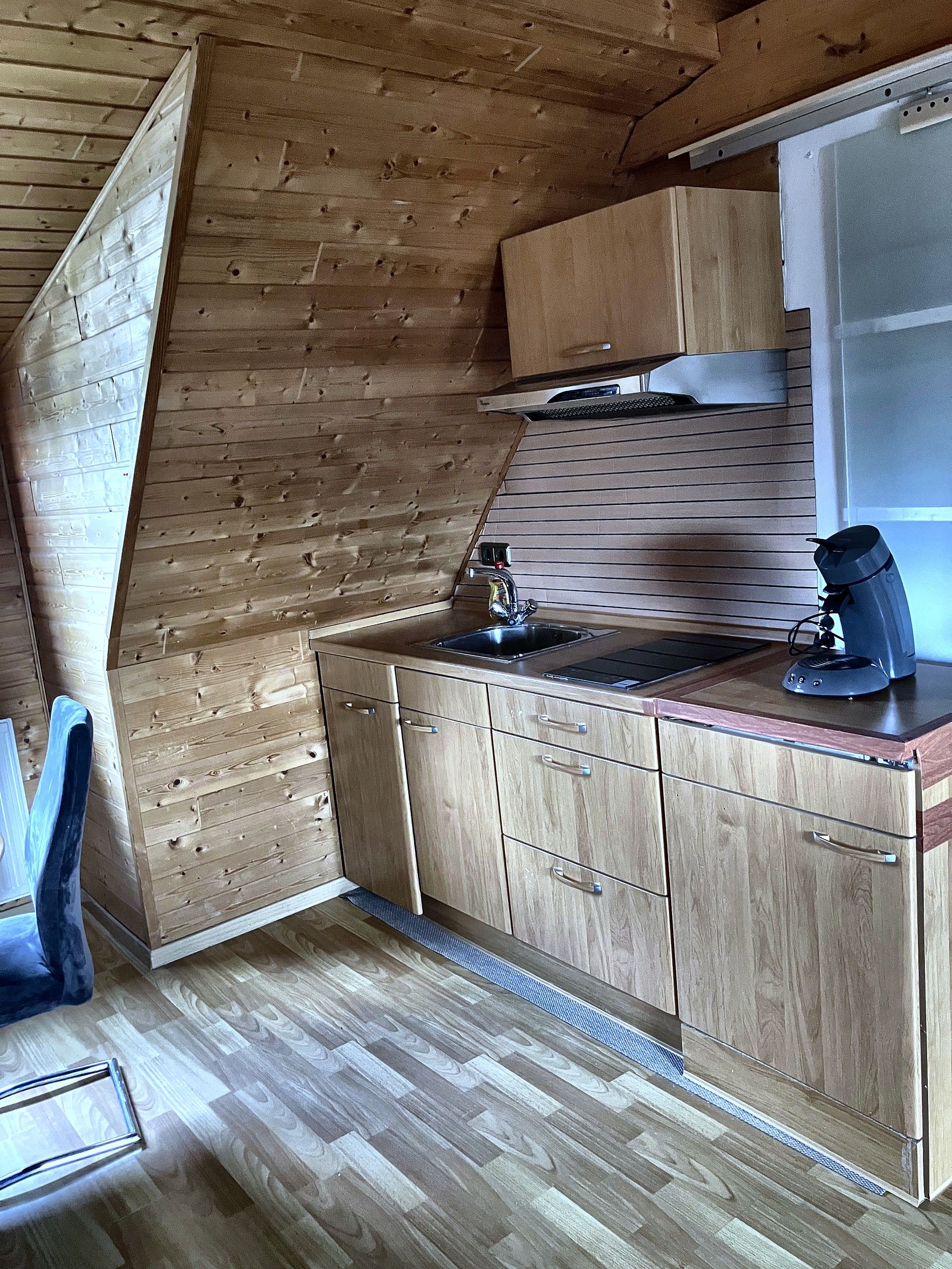 Een kleine keuken met houten kastjes, een spoelbak en een raam.
