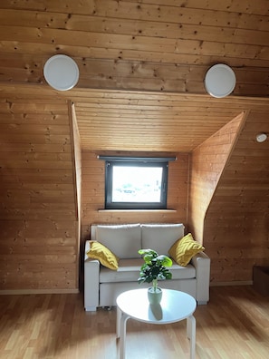 Ein gemütliches Zimmer mit Holzbalkendecke, einer Couch mit Kissen, einem kleinen Tisch und einem Fenster mit Ausblick.