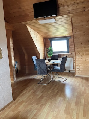 Ein Essbereich mit Tisch und Stühlen, einer Topfpflanze und einem Fenster mit Tageslicht.