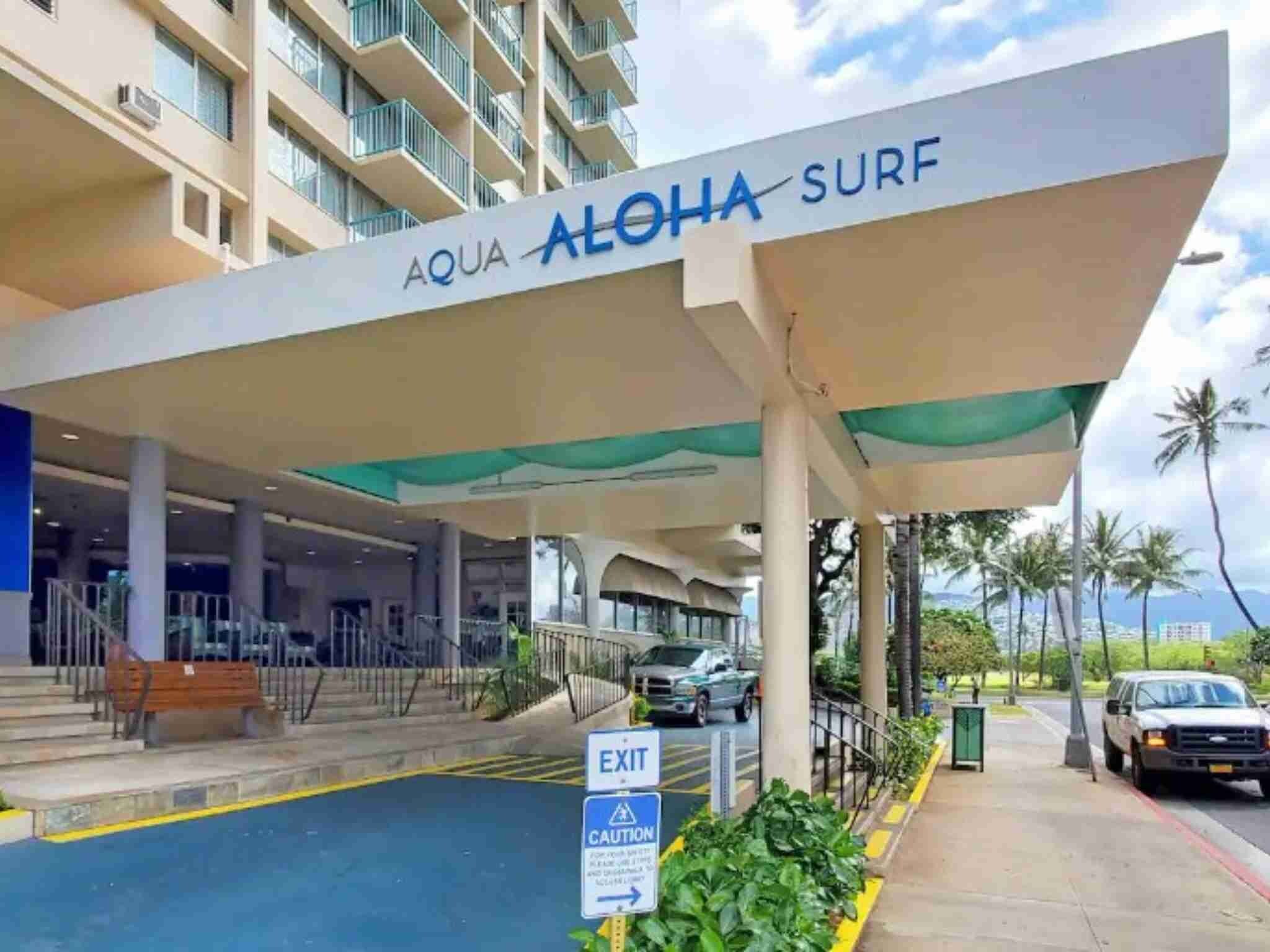 A hotel entrance with an 'EXIT' sign, a caution sign, and a covered area with a view of palm trees.