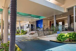 A modern building with a covered entrance, palm trees, and a blue sign. - Aloha Surf 504 - Cozy studio in serene Honolulu Near Canal with refreshing AC (Honolulu)