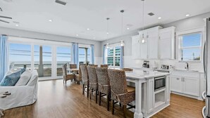 A modern kitchen with white cabinets, a dining area with patterned chairs, and a view of the ocean through large windows. - Chat N Chill Beach Retreat Pool, Beachfront, Private Beach (Panama City Beach)