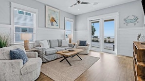 A spacious living room with a grey sofa, a coffee table, and a view of the beach through large glass doors. - Chat N Chill Beach Retreat Pool, Beachfront, Private Beach (Panama City Beach)