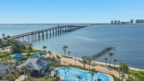 A coastal resort with a long pier extending into the water, a swimming pool, and a beach area with palm trees. - New 2026 listing! Pool, private balcony with big water views, steps to the beach (Navarre Beach)