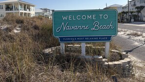 A welcome sign for Navarre Beach, Florida, with a clear sky and residential buildings in the background. - New 2026 listing! Pool, private balcony with big water views, steps to the beach (Navarre Beach)