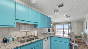 A kitchen with turquoise cabinets, a granite countertop, and a window with a view of the beach. - New 2026 listing! Pool, private balcony with big water views, steps to the beach (Navarre Beach)