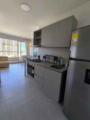 A modern kitchen with grey cabinets, a stainless steel refrigerator, and a gas stove. - Apto Lujo Frente al Mar | Relájate en Santa Marina (Urb Don Jaca)