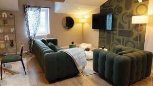 Un salon moderne avec un canapé d’angle, un pouf assorti, un téléviseur à écran plat fixé au mur et une lampe sur pied.