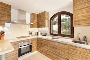 Eine moderne Küche mit Holzausstattung, Edelstahlgeräten und einem großen Fenster mit Blick auf Grünflächen.