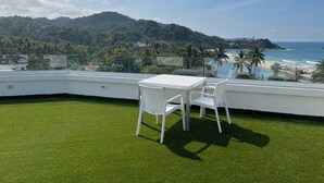 Ein Balkon mit weißem Tisch und Stühlen, der Blick auf einen Strand und eine Berglandschaft freigibt.