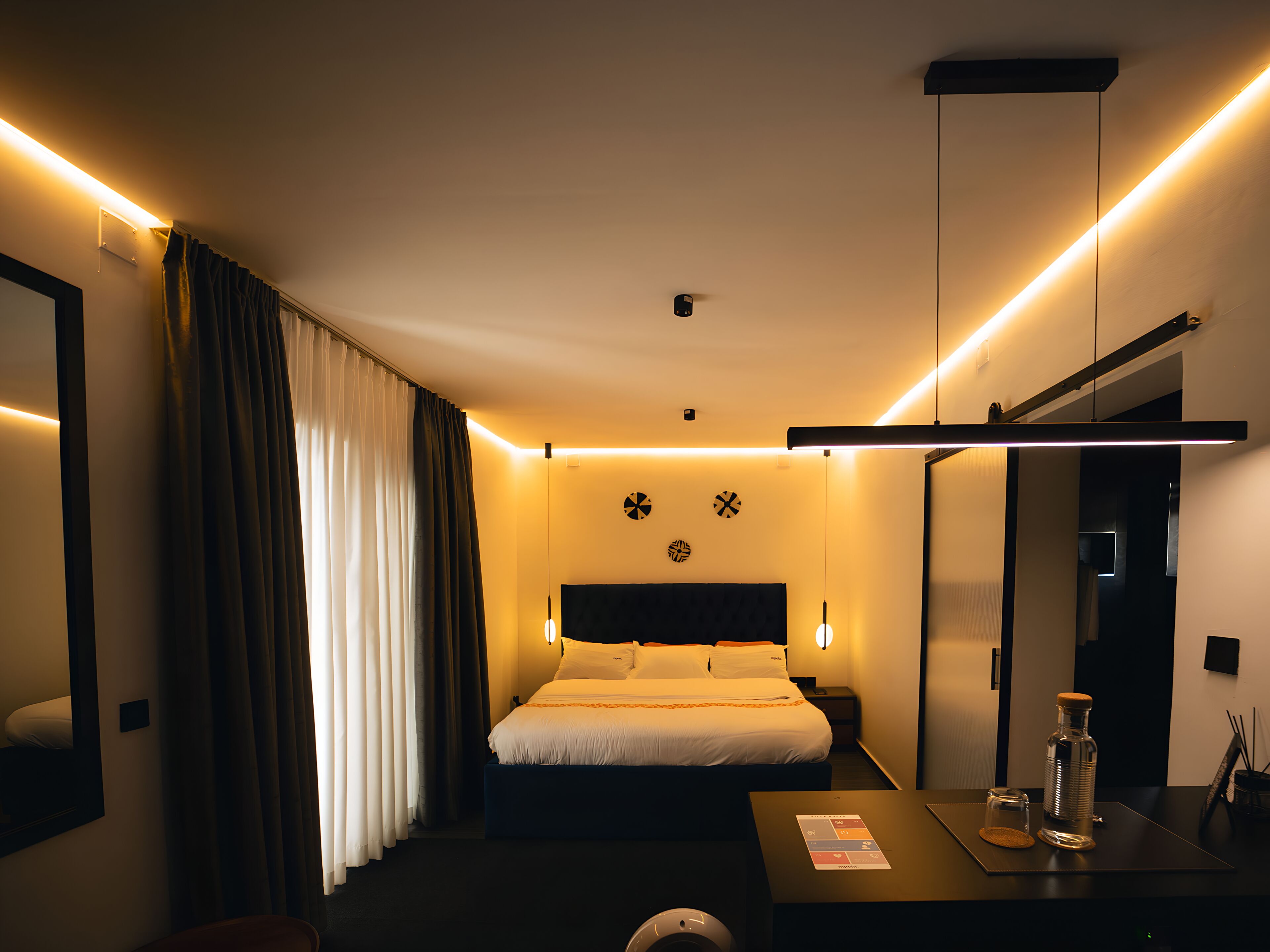 A modern hotel room with a bed, bedside table, and a mirror.