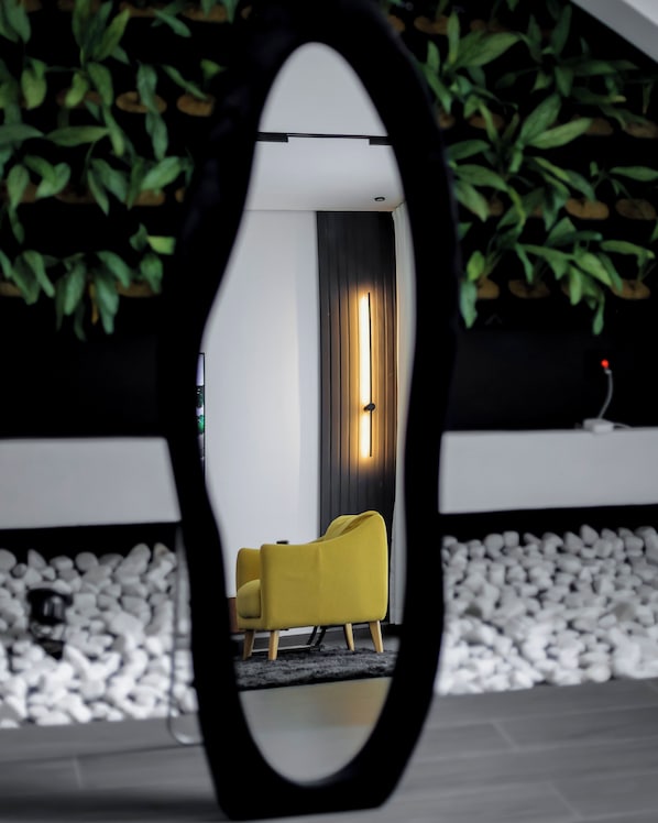 Un miroir reflétant une pièce avec un fauteuil jaune, un rideau sombre et un mur végétal.