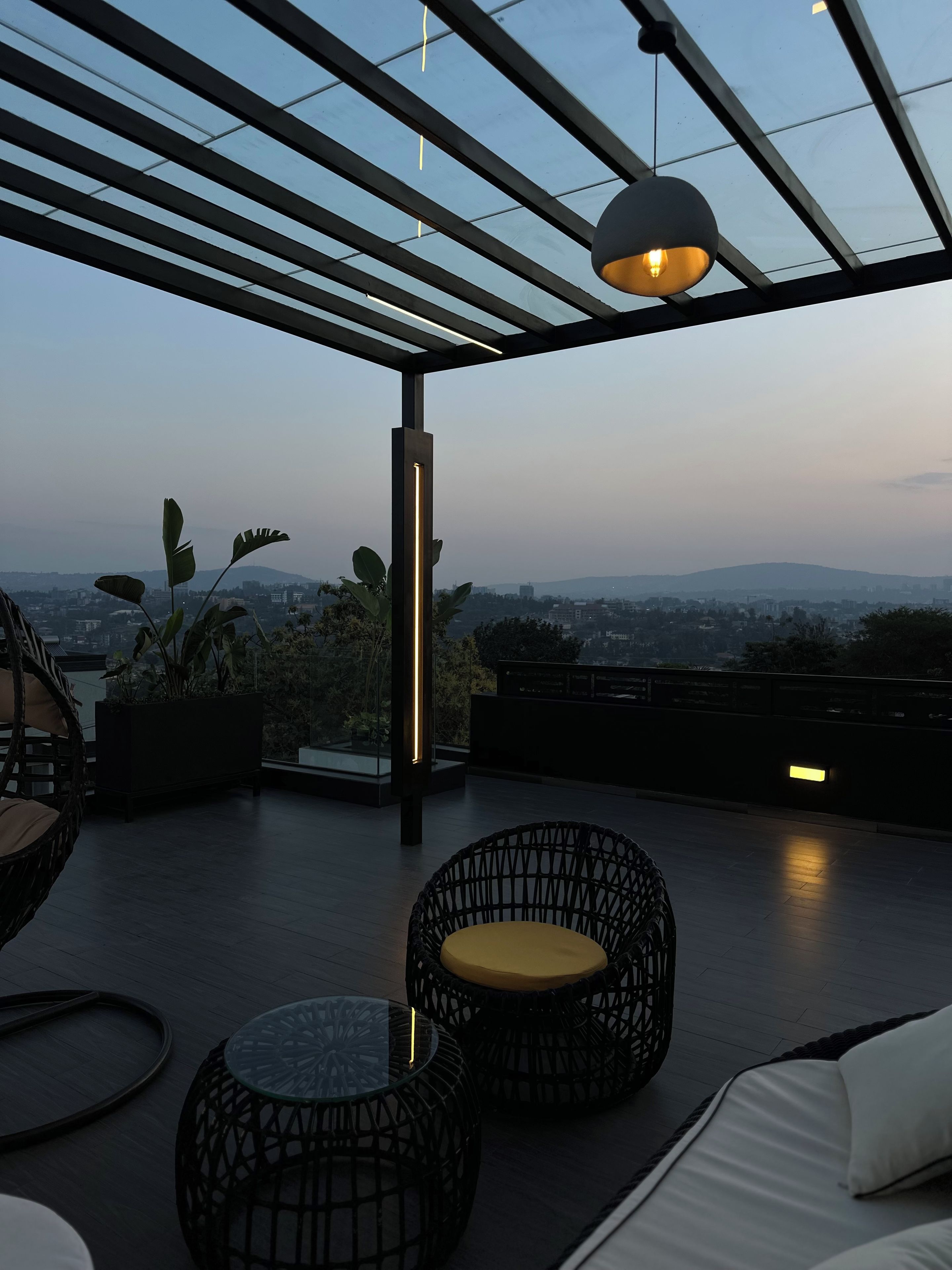 Una terraza en la azotea con vistas al paisaje urbano, que incluye una pérgola, un área de estar con sillas de mimbre y una mesa de vidrio.