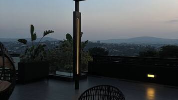 Una terraza en la azotea con vistas al paisaje urbano, que incluye una pérgola, un área de estar con sillas de mimbre y una mesa de vidrio.
