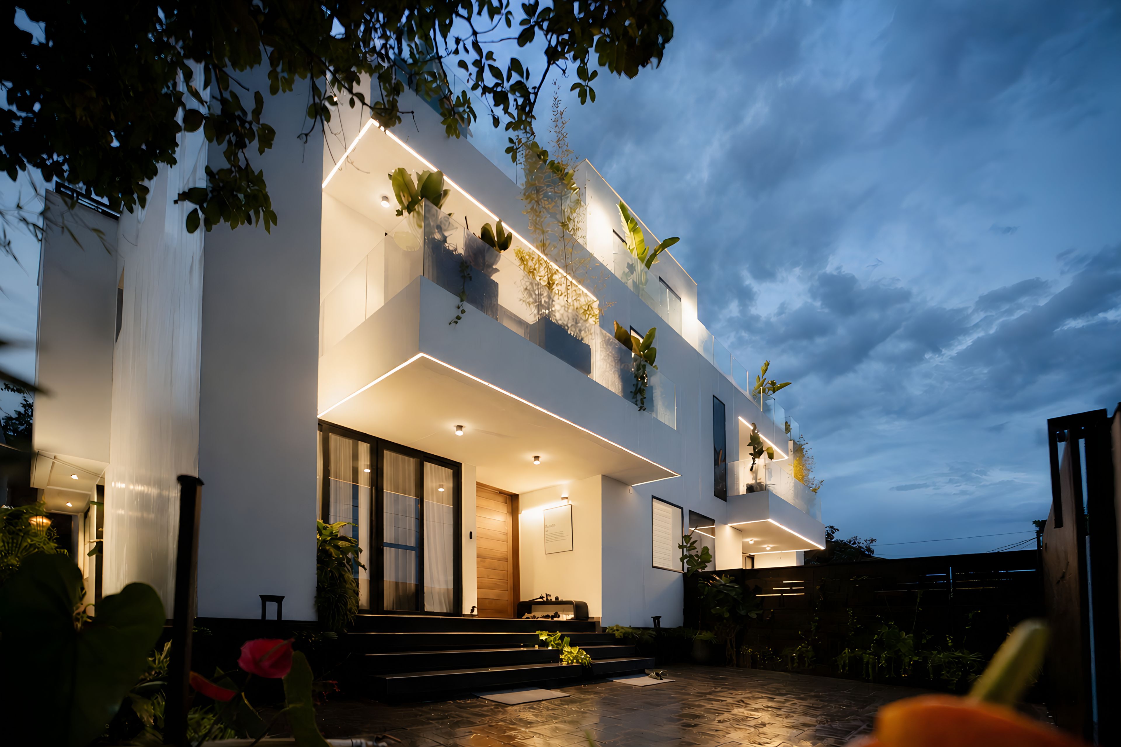 A modern two-story house with a balcony, large windows, and outdoor lighting.