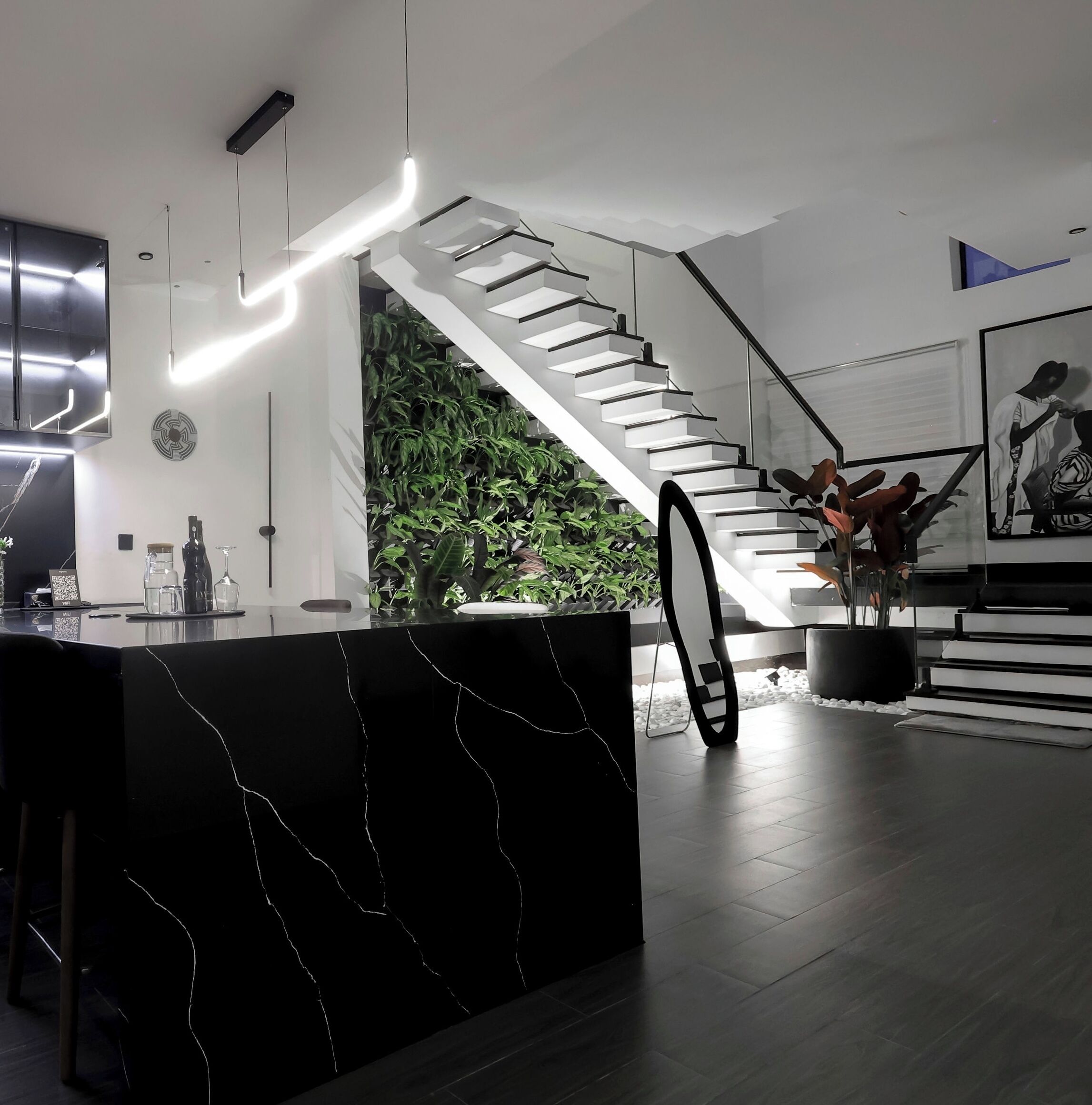 A modern kitchen with a black marble countertop, a staircase with a glass railing, and a wall-mounted TV.