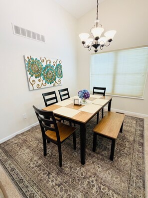 A dining area with a wooden table, black chairs, a chandelier, a patterned rug, and a decorative wall piece.