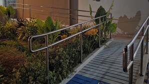 Un escalier avec des rampes en métal, un chemin pavé bleu conçu pour les personnes malvoyantes, et une variété de plantes d’intérieur.
