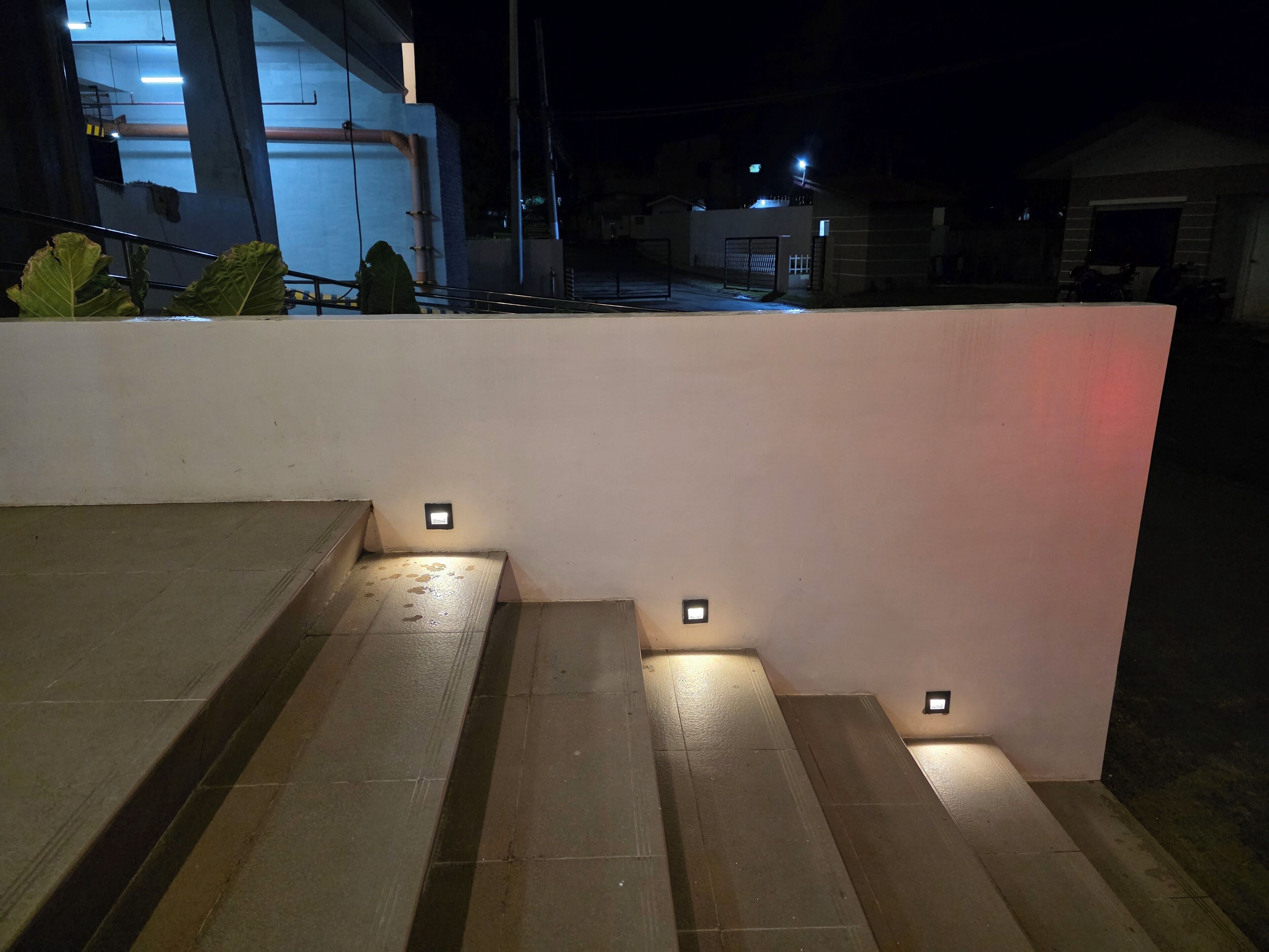 Una serie de escalones exteriores con luces pequeñas en la parte superior, que conducen a una pared blanca.
