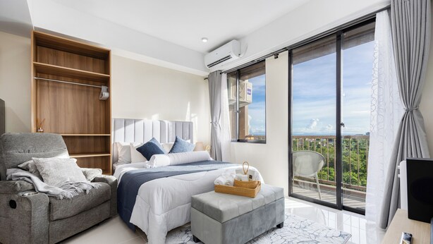 Une chambre moderne avec un lit, un canapé, un petit pouf, une armoire et un balcon avec vue.