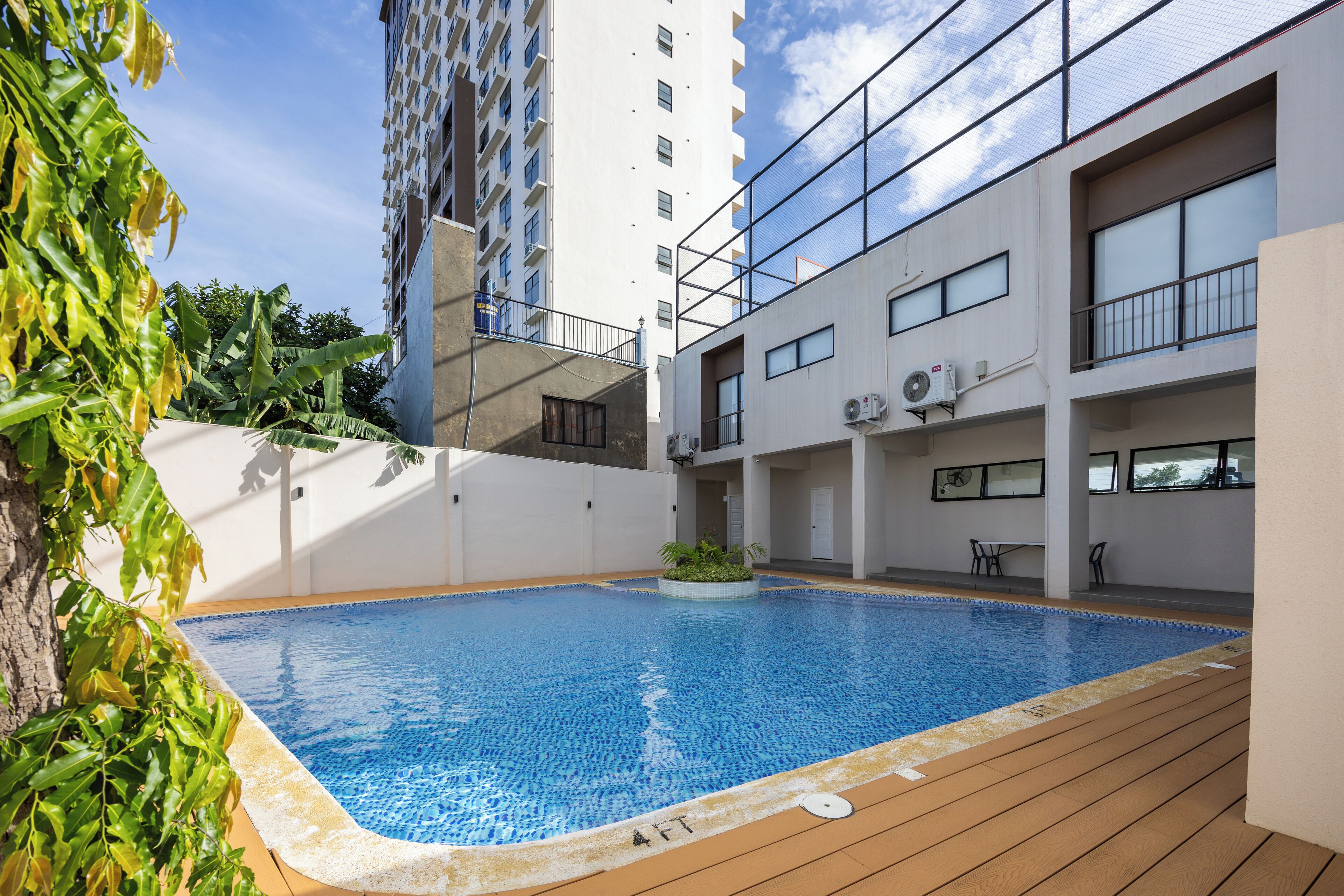 Un edificio moderno con piscina en la azotea, rodeado de vegetación y un cielo despejado.