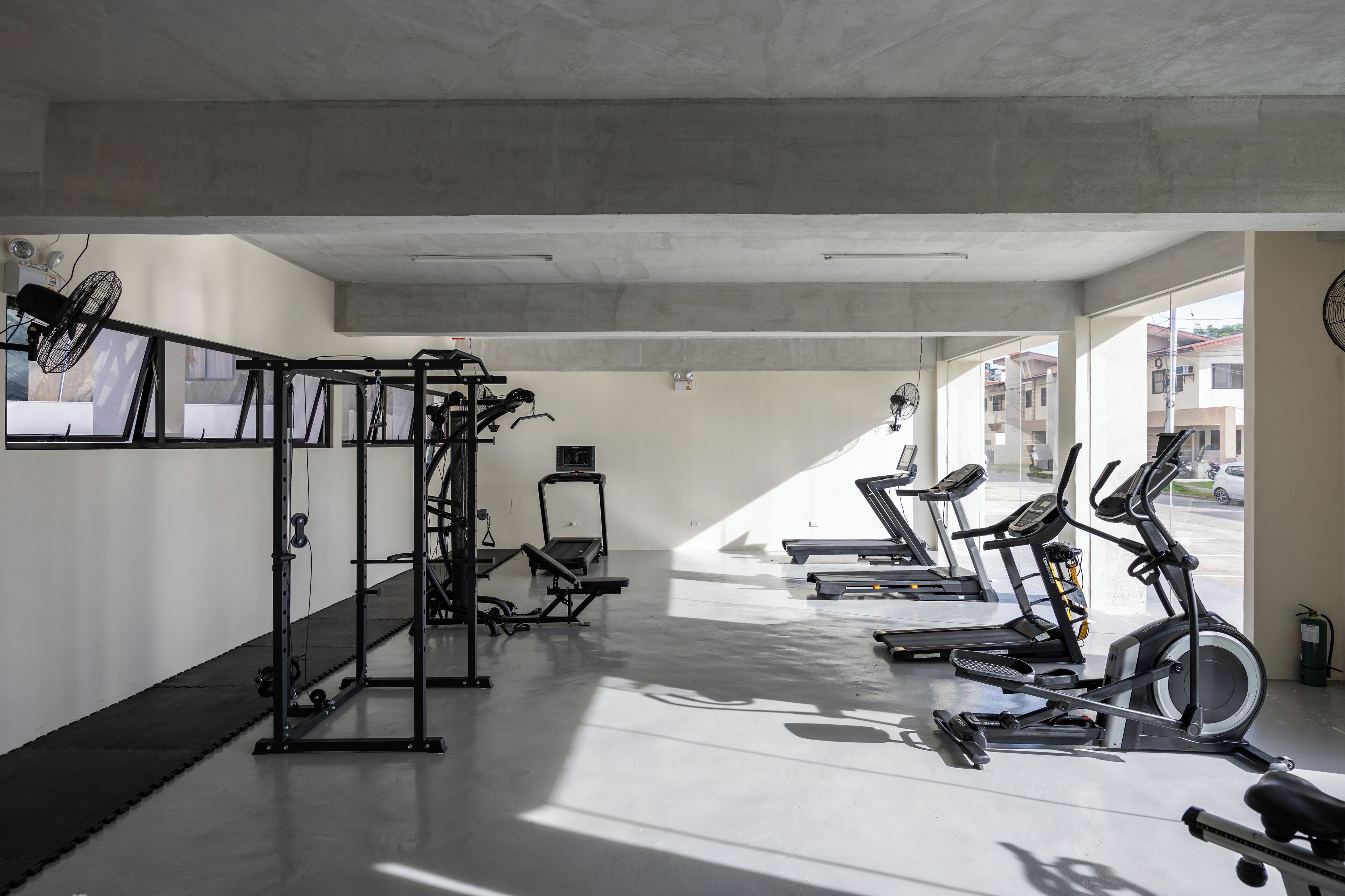 Un gimnasio con diversos equipos de ejercicio, incluyendo cintas de correr, una elíptica y una máquina de pesas.