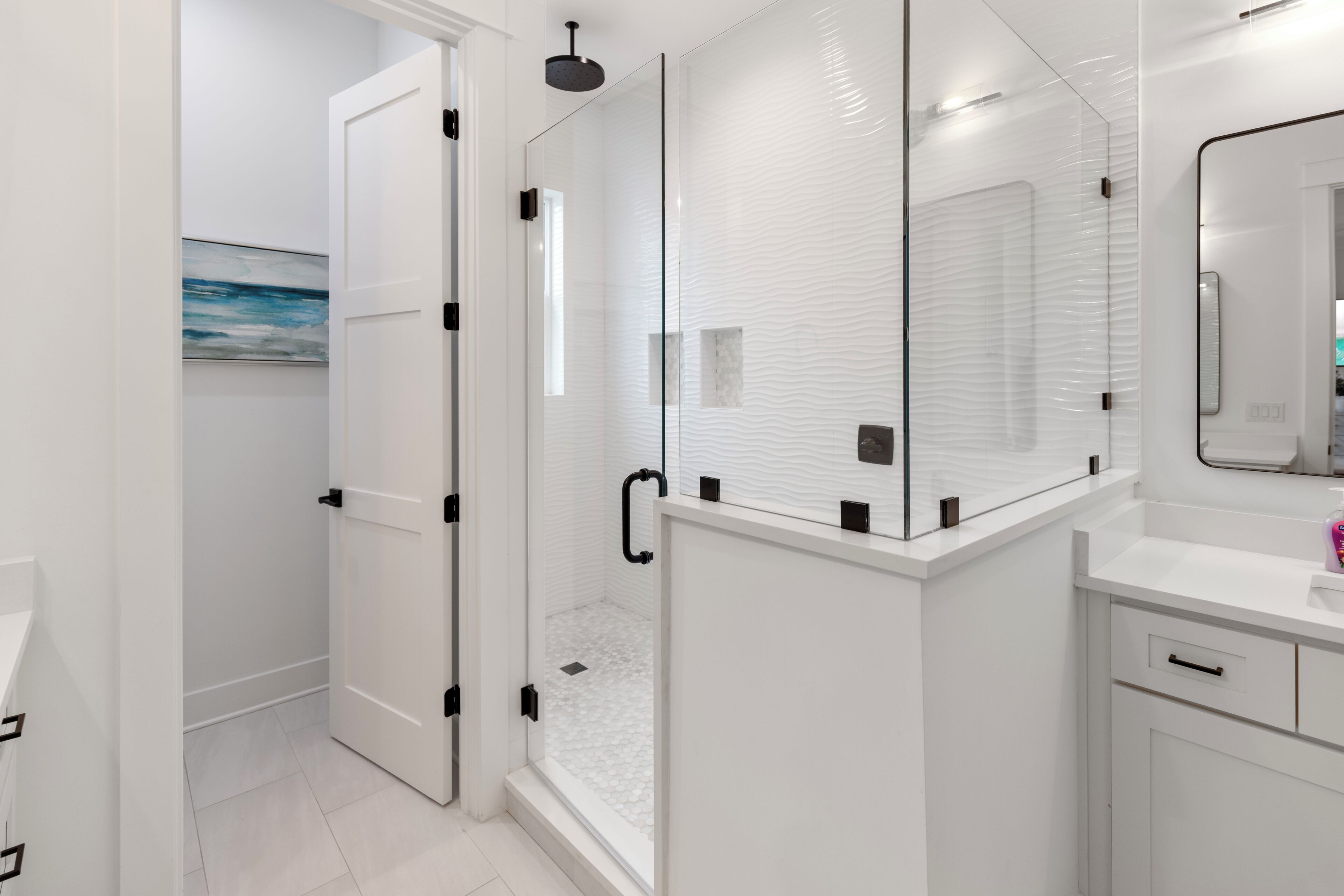 A modern bathroom with a glass shower enclosure, white tiled walls, and a minimalist design.