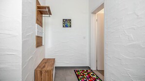 A hallway with white textured walls, a wooden bench, a colorful rug, and a framed artwork on the wall.