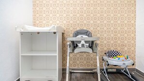 A room with a white shelf unit, a high chair, and a walker.
