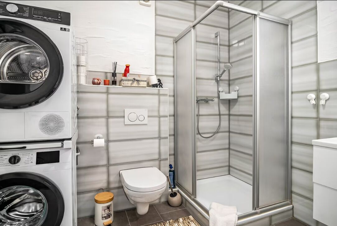 Ein kleines Badezimmer mit Waschmaschine, Toilette und Duschkabine.