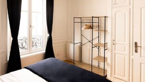 Een slaapkamer met een bed, een raam met donkere gordijnen, een radiator en een metalen garderobe met planken.