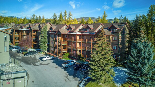 A multi-story lodge with balconies, a parking area, and surrounding trees. - Cozy Kimberley Condo with Private Hot Tub (Kimberley)