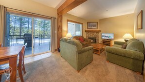 A cozy living room with a fireplace, green sofas, a coffee table, and a TV. - Cozy Kimberley Condo with Private Hot Tub (Kimberley)