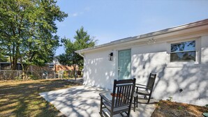 A single-story house with a white exterior, a green door, and two rocking chairs in the front yard. - King bed, EV charger, minutes from UNCW, ILM Airport, area beaches and downtown. (Wilmington)