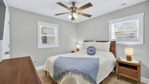 A bedroom with a bed, nightstands, a ceiling fan, and windows with blinds. - King bed, EV charger, minutes from UNCW, ILM Airport, area beaches and downtown. (Wilmington)