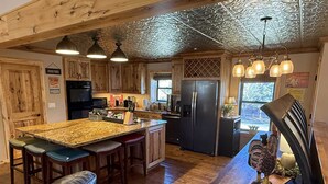 A kitchen with wooden cabinets, a central island with stools, a refrigerator, and pendant lighting. - Restoration of the Rockies- Great Cabin Close to Town with Room for All (Lake City)