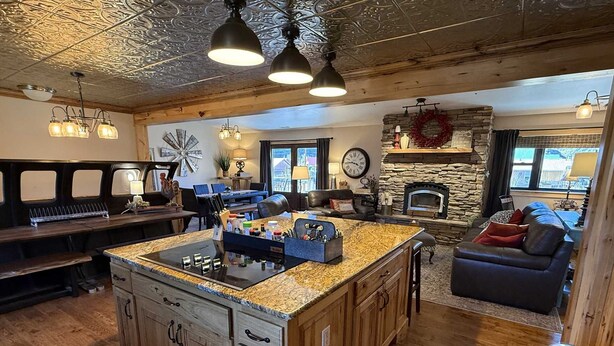 A spacious kitchen with a large island, wooden cabinets, and a stone fireplace. - Restoration of the Rockies- Great Cabin Close to Town with Room for All (Lake City)
