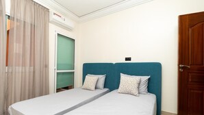Quarto com duas camas de solteiro, uma porta de madeira e uma janela com cortinas.