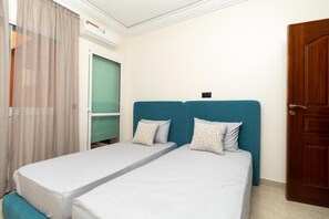 Ein Zimmer mit zwei Einzelbetten, einer Holztür und einem Fenster mit Vorhängen.