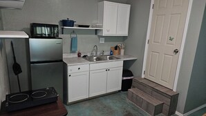 Una cocina compacta con armarios blancos, microondas integrado, un lavabo y una pequeña encimera con estufa.