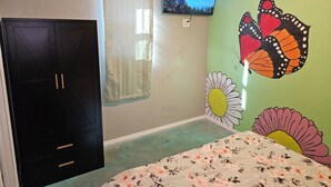 Un dormitorio con una cama, un armario, un televisor y una pared con un mural de mariposa.