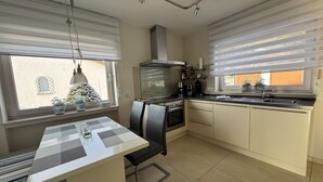 A modern kitchen with a central island, a built-in oven, and a dishwasher. There are potted plants on the windowsill and a view of the outside. - Modern, well-equipped 5* vacation apartment on the sunny side of Linz am Rhein (Linz am Rhein)
