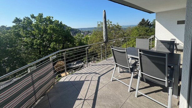 A balcony with a table and chairs, a metal railing, and a view of a town and hills. - Modern, well-equipped 5* vacation apartment on the sunny side of Linz am Rhein (Linz am Rhein)
