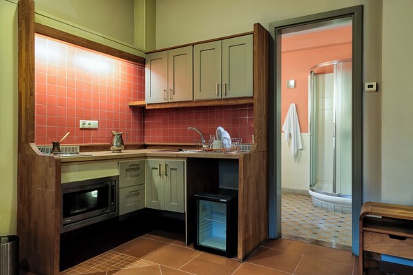 A compact kitchen with a microwave, oven, and sink. A small refrigerator is located near the sink. The kitchen features wooden cabinets and a tiled backsplash. - Taleton Eco Guesthouse (Sparta)