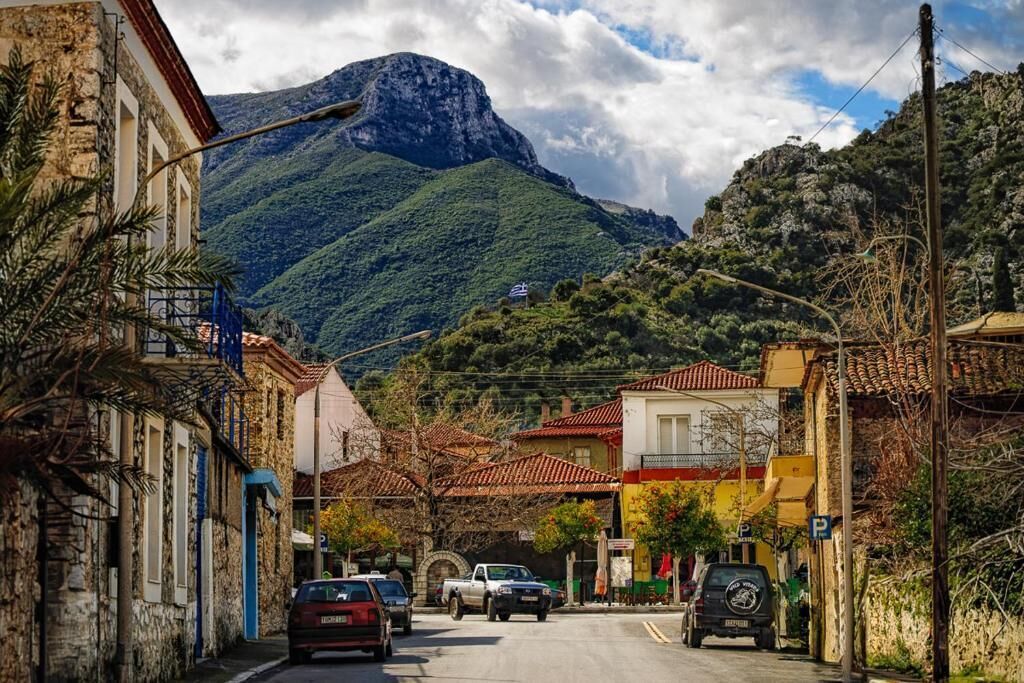 A street view with buildings, parked cars, and a mountain in the background.
